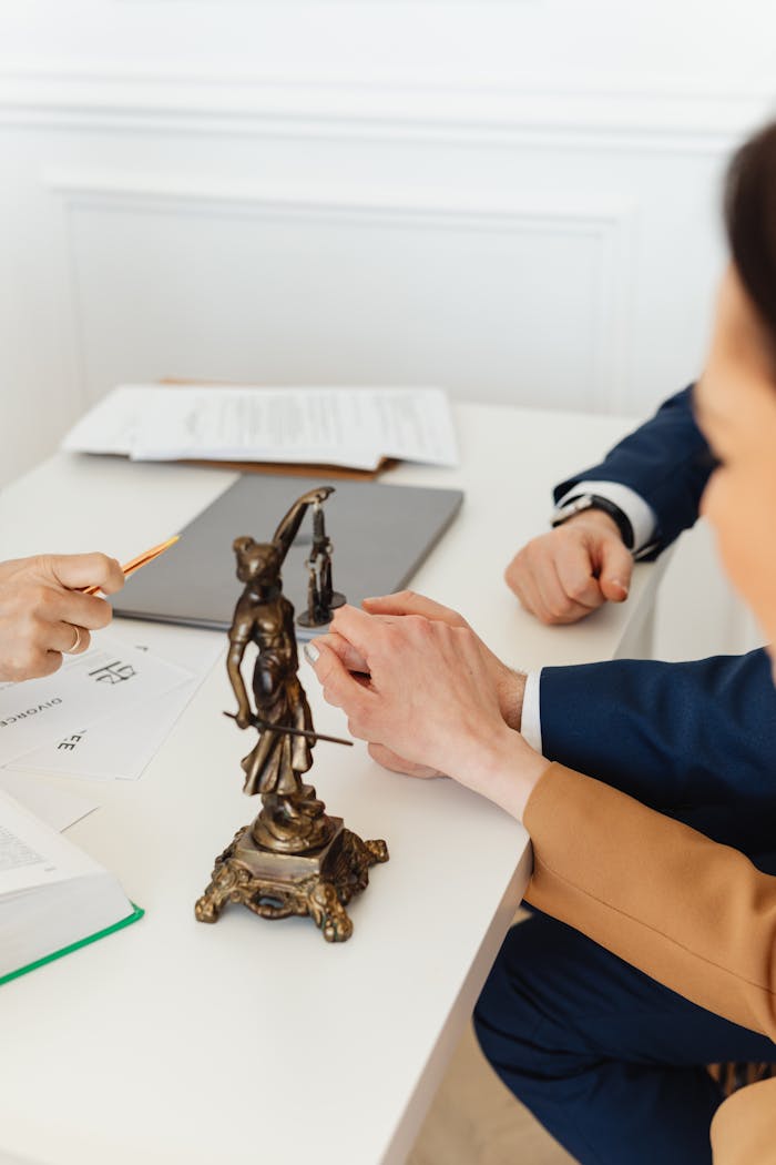 Legal professionals discussing documents with Lady Justice statue on desk.